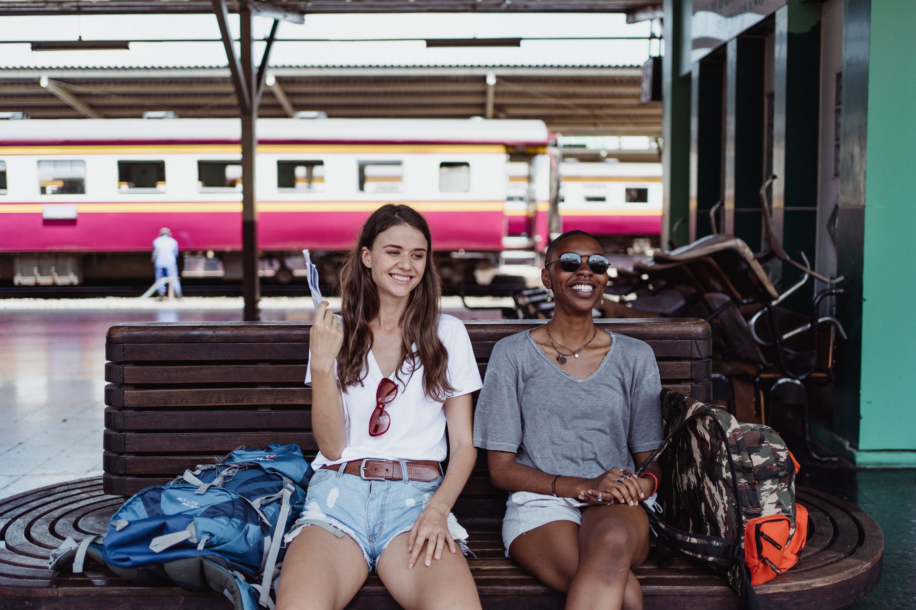 women sitting on a bench on a train platform and smiling