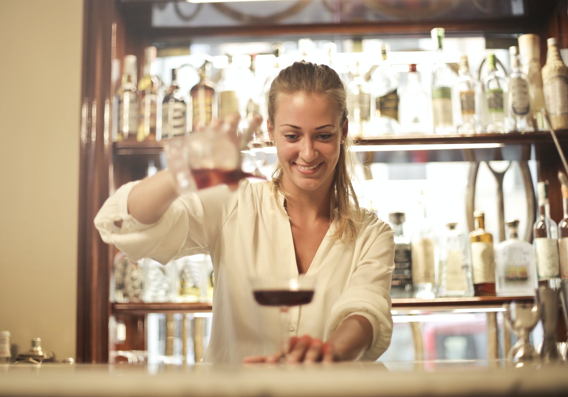 cheerful female bartender pouring cocktail in bar