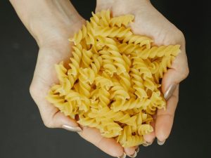 crop woman showing heap of raw pasta