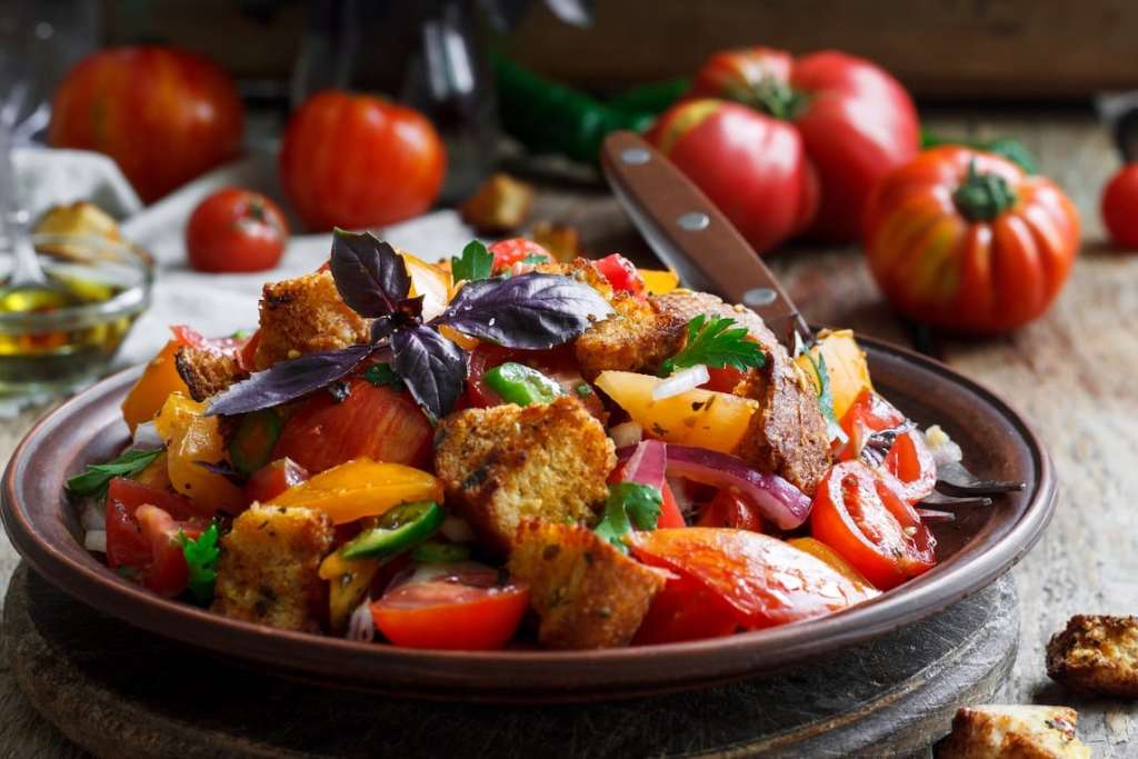 Eine traditionelle Brotsalat-Schüssel mit frischen Tomaten, Paprika, Zwiebeln und knusprigen Brotwürfeln, garniert mit frischem Basilikum und Petersilie.